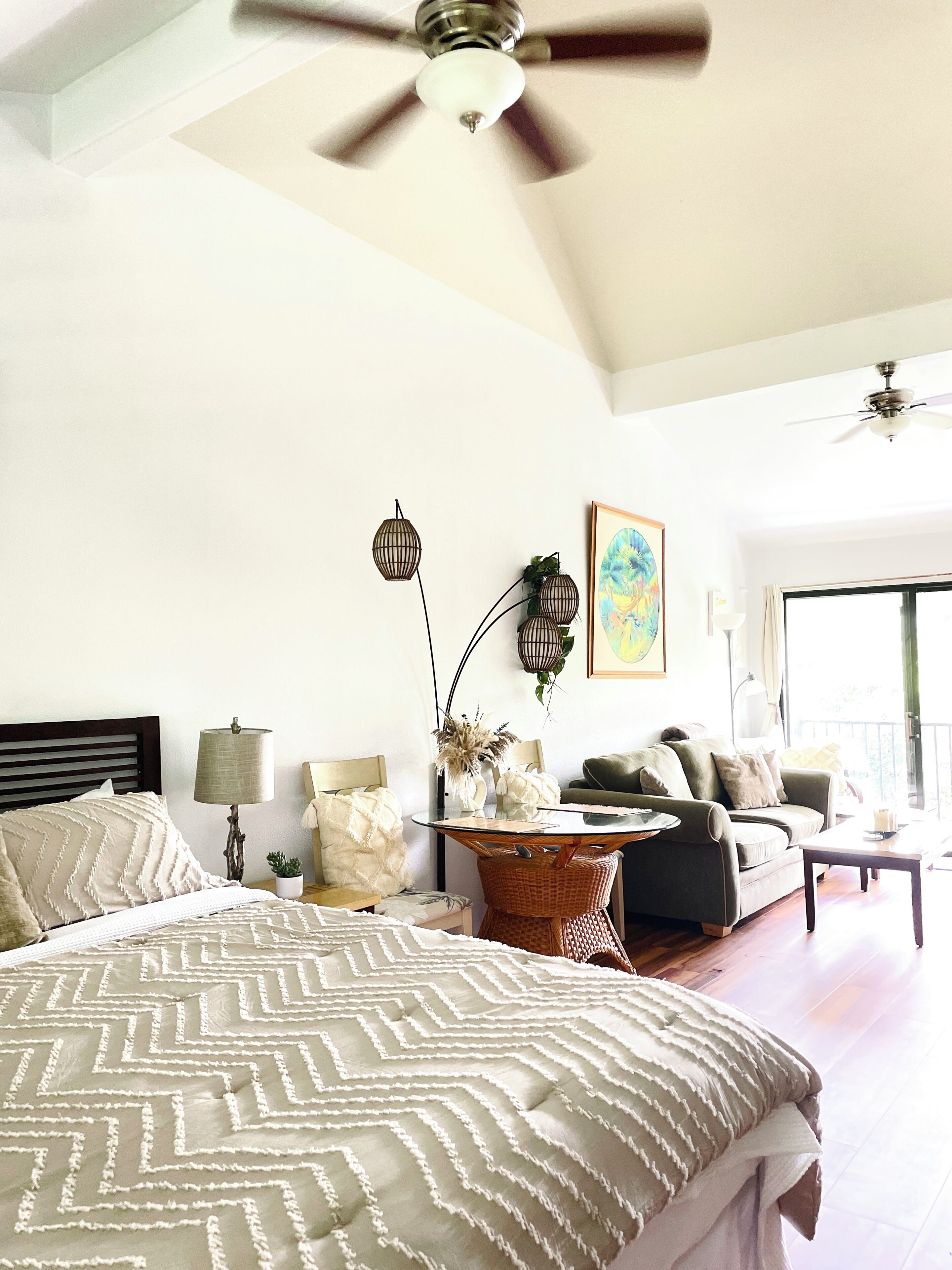 A bedroom with a bed, a sofa, a dining table, and a ceiling fan.