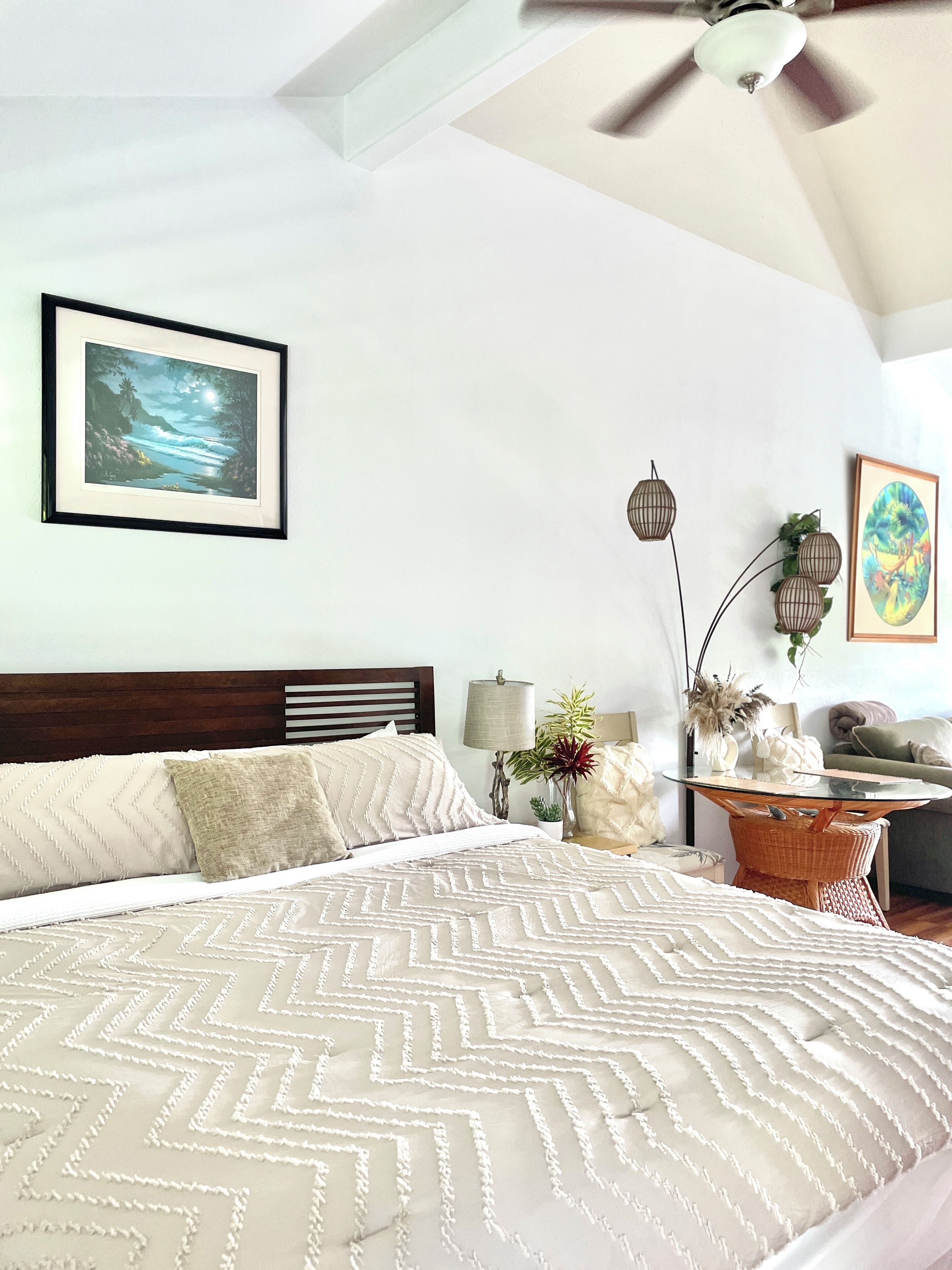 A bedroom with a bed, a ceiling fan, a nightstand, a lamp, and wall art.