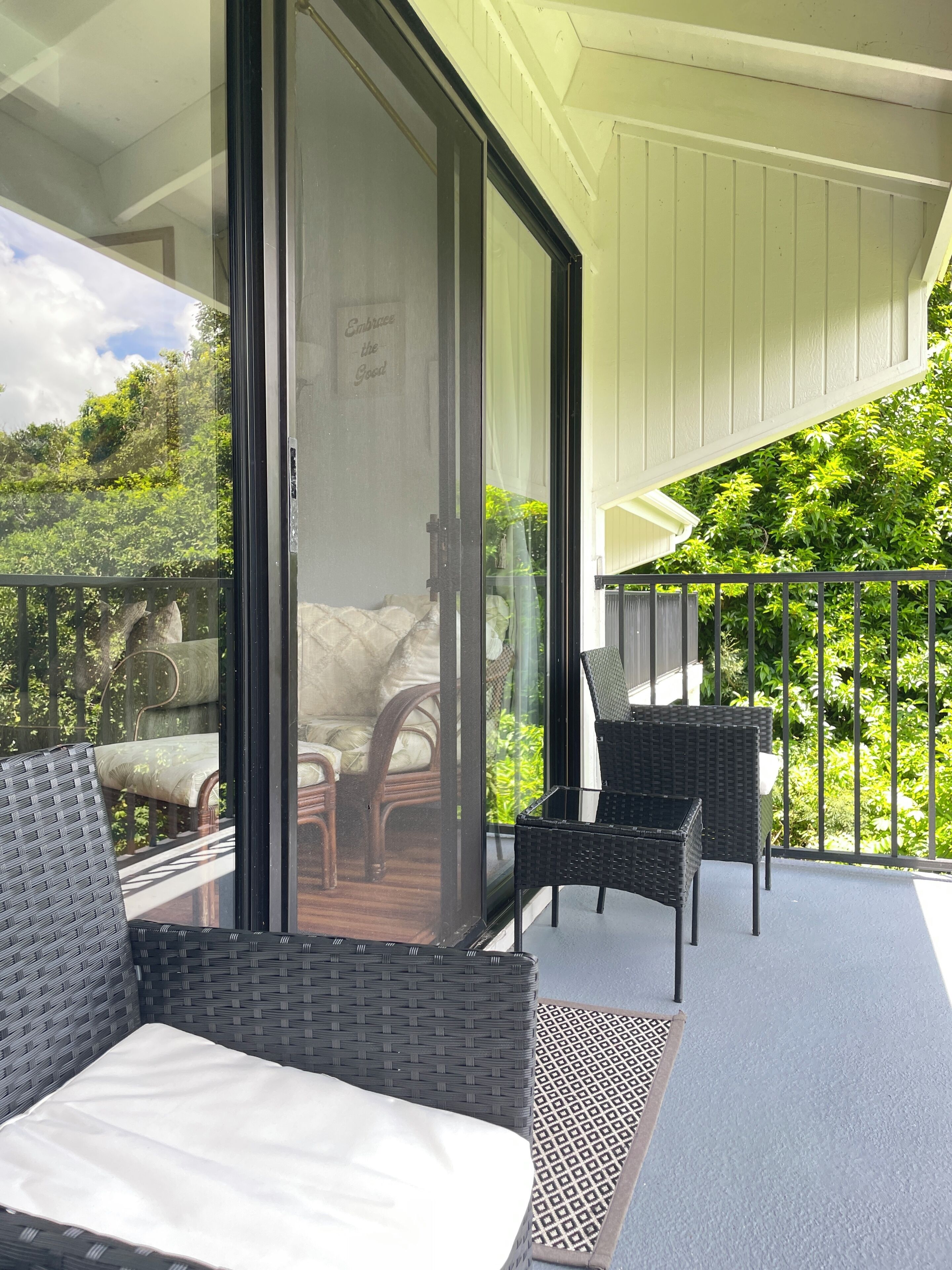 A balcony with wicker furniture, a glass door, and a view of greenery.