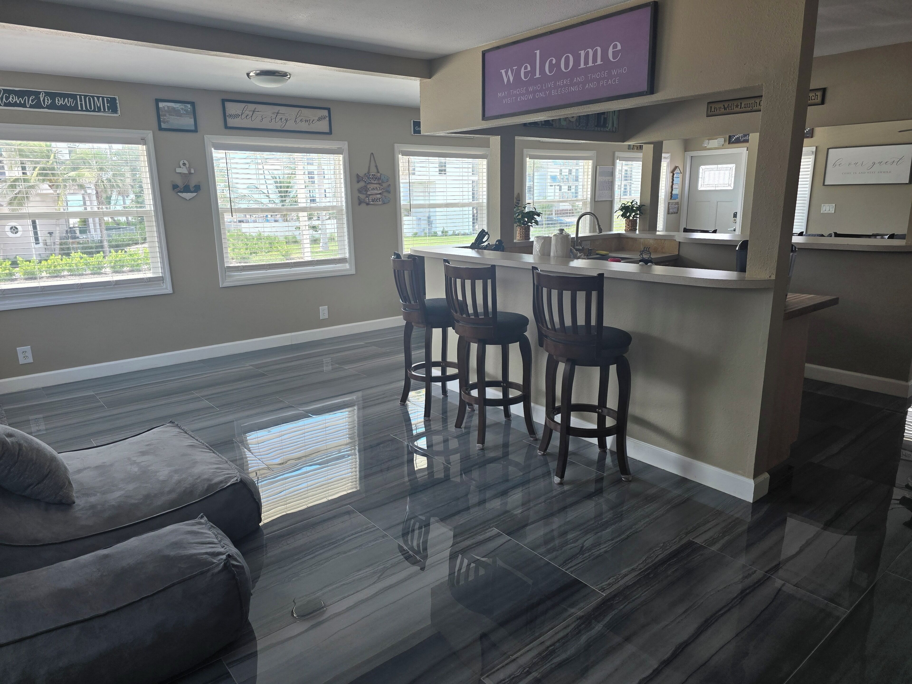 A modern kitchen with a bar area, large windows, and a welcome sign.