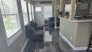 A spacious living area with a dark marble floor, a grey sofa, and a kitchen area with a countertop and a hanging plant. - BRAND NEW 16x14 Heated Swim Jacuzzi Sleeps 8 Beach Front! No Condo Park 4 Cars! (Fort Myers Beach)