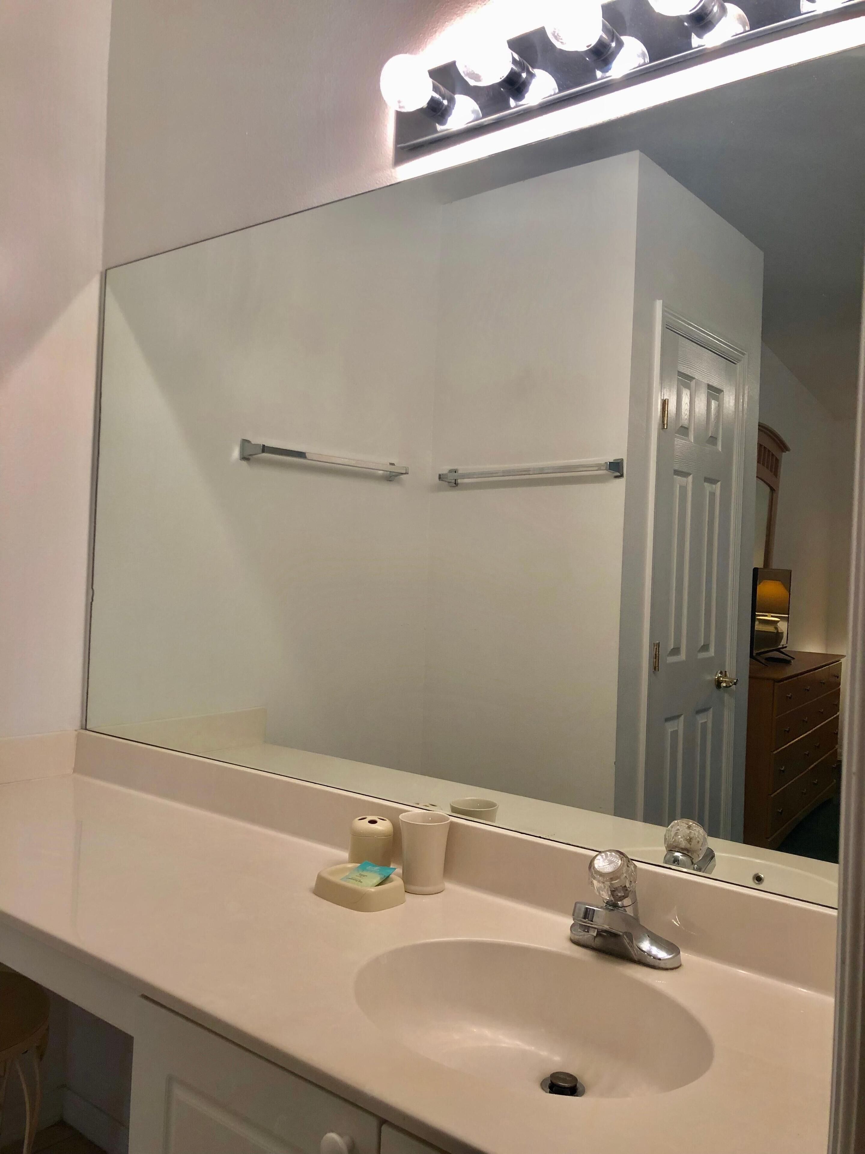 A bathroom with a large mirror, a sink, and a vanity.
