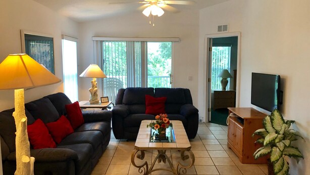 A living room with a sofa, a coffee table, a lamp, a television, and a plant. - Three Bedroom Condo - 8841 GP - Vusa (Kissimmee)