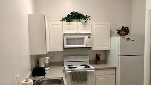 A modern kitchen with white cabinets, a stainless steel sink, a microwave, a stove, and a refrigerator. - Three Bedroom Condo - 8841 GP - Vusa (Kissimmee)