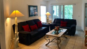 A living room with two sofas, a coffee table, and two lamps. There is a ceiling fan and a window with blinds. - Three Bedroom Condo - 8841 GP - Vusa (Kissimmee)