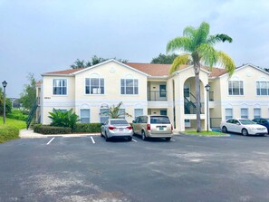 A multi-story building with a parking lot, featuring a staircase and a palm tree.