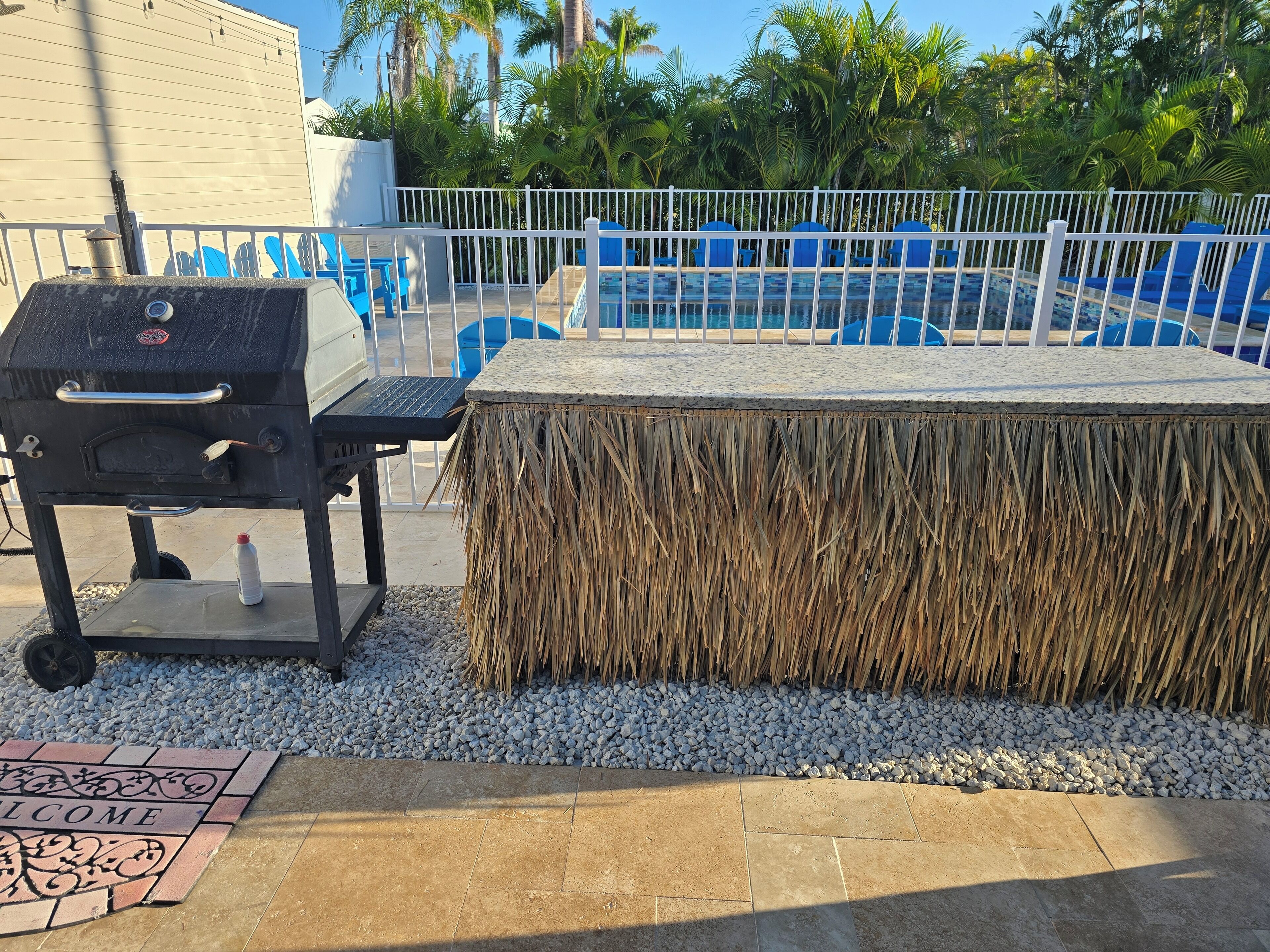 Un barbecue, une table en osier et un espace piscine avec des chaises bleues.