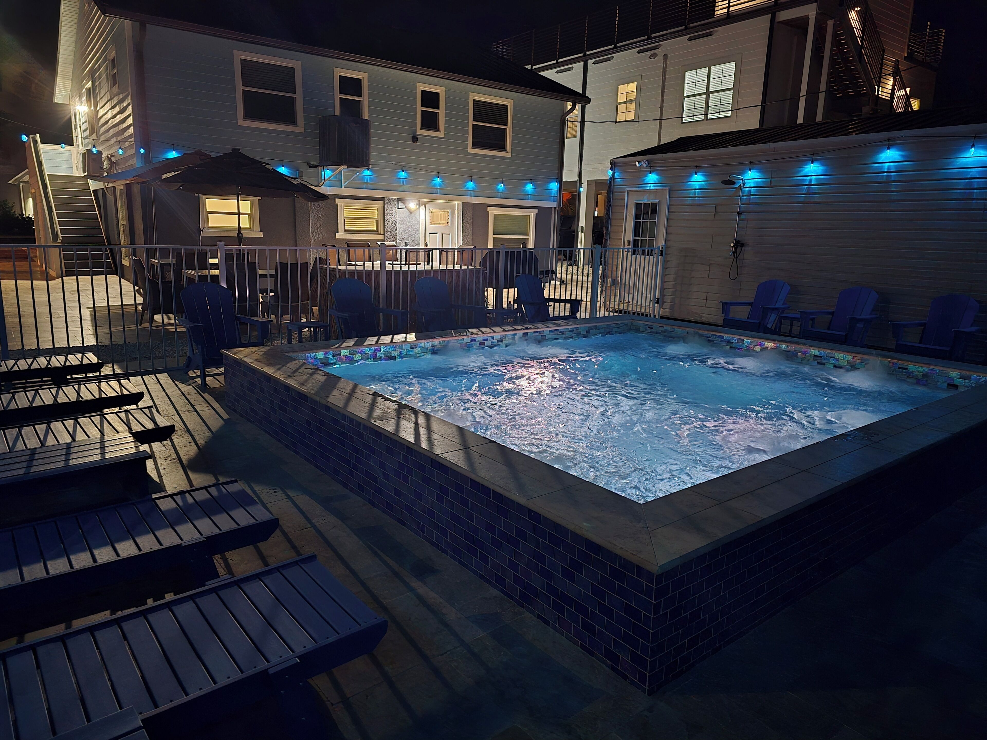 A hot tub surrounded by deck chairs and a covered patio area.