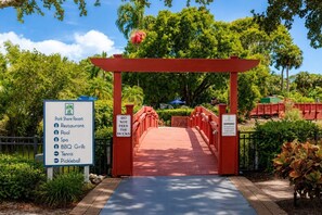 Un arco rojo que da paso a un parque con un cartel que enumera servicios como restaurante, piscina, spa, parrillas, tenis y pádel.