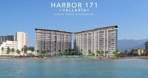 A modern hotel with a prominent 'Harbor 171 - Vallarta' sign, featuring a two-story structure with balconies, situated by a beach with palm trees and a clear blue sky.