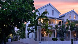 A two-story house with a balcony, surrounded by a white picket fence, and palm trees in the foreground. - Eisenhower Retreat (Key West)