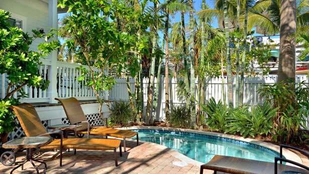 A poolside area with lounge chairs, a small table, and a white fence. - Eisenhower Retreat (Key West)