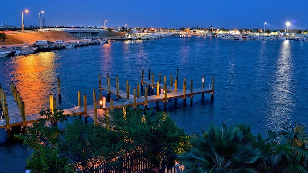 A marina at dusk with boats docked, wooden piers, and a distant cityscape. - Island Chi c (Key West)