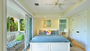 A bedroom with a large bed, a ceiling fan, a window with blinds, a nightstand, and a bench with a cushion. - Island Chi c (Key West)