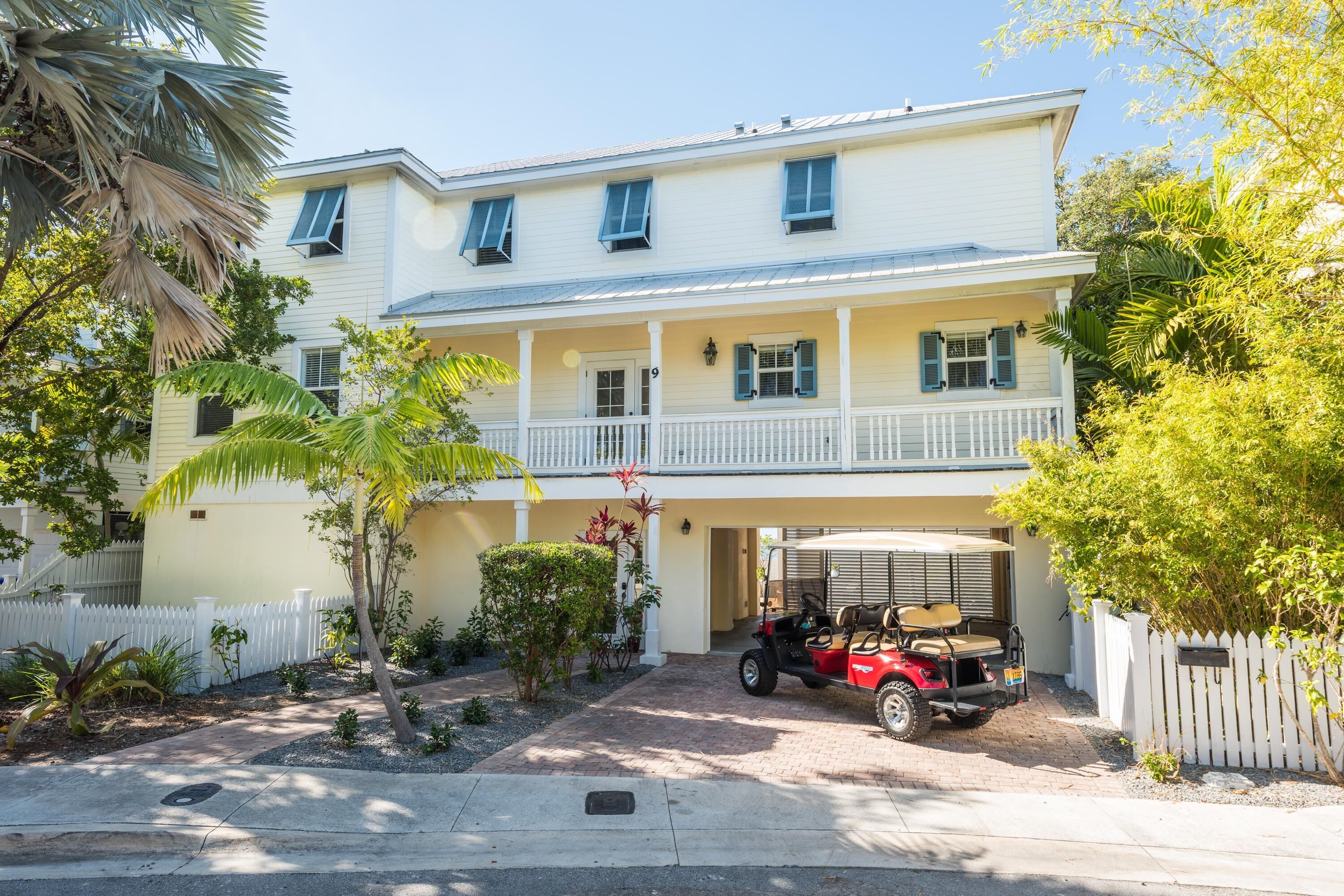 Une maison à deux étages avec un porche couvert et une voiturette de golf rouge garée devant.