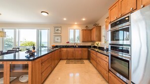 A modern kitchen with wooden cabinets, a black countertop, stainless steel appliances, and a large window providing a view of the outdoors. - 3 4 Tim e (Key West)