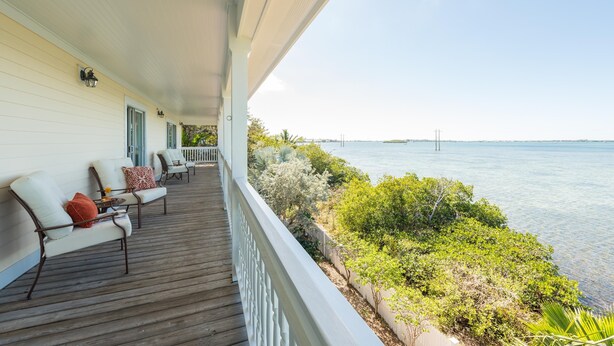 A wooden deck with outdoor seating, overlooking a body of water and a distant bridge. - 3 4 Tim e (Key West)