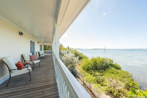 A wooden deck with outdoor seating, overlooking a body of water and a distant bridge. - 3 4 Tim e (Key West)