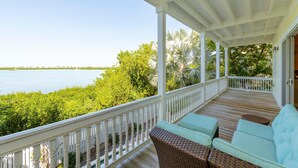 A covered porch with a view of the water, a wicker sofa, and a white railing. - Banana Breez e (Key West)