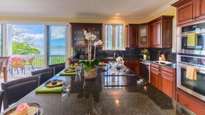 A kitchen with a large island, dark countertops, wooden cabinets, and stainless steel appliances. - Southern Comfor t (Key West)