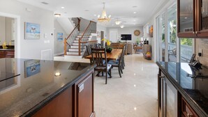 A spacious kitchen with a central island, a dining area with chairs, a staircase, and a large window offering a view of the outdoors. - Southern Comfor t (Key West)