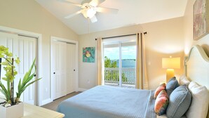 A bedroom with a bed, a ceiling fan, a window with curtains, a painting on the wall, and a plant on the nightstand. - Seaside Retreat (Key West)