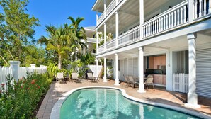 A pool area with a white fence, palm trees, and a two-story building with balconies. - Seaside Retreat (Key West)