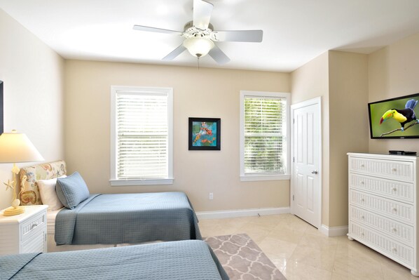 A bedroom with two beds, a ceiling fan, a television, and a dresser. - Coastal Comfort (Key West)