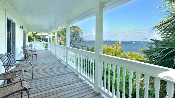A covered porch with white railings and wooden flooring, overlooking a body of water with distant boats. - Coastal Comfor t (Key West)