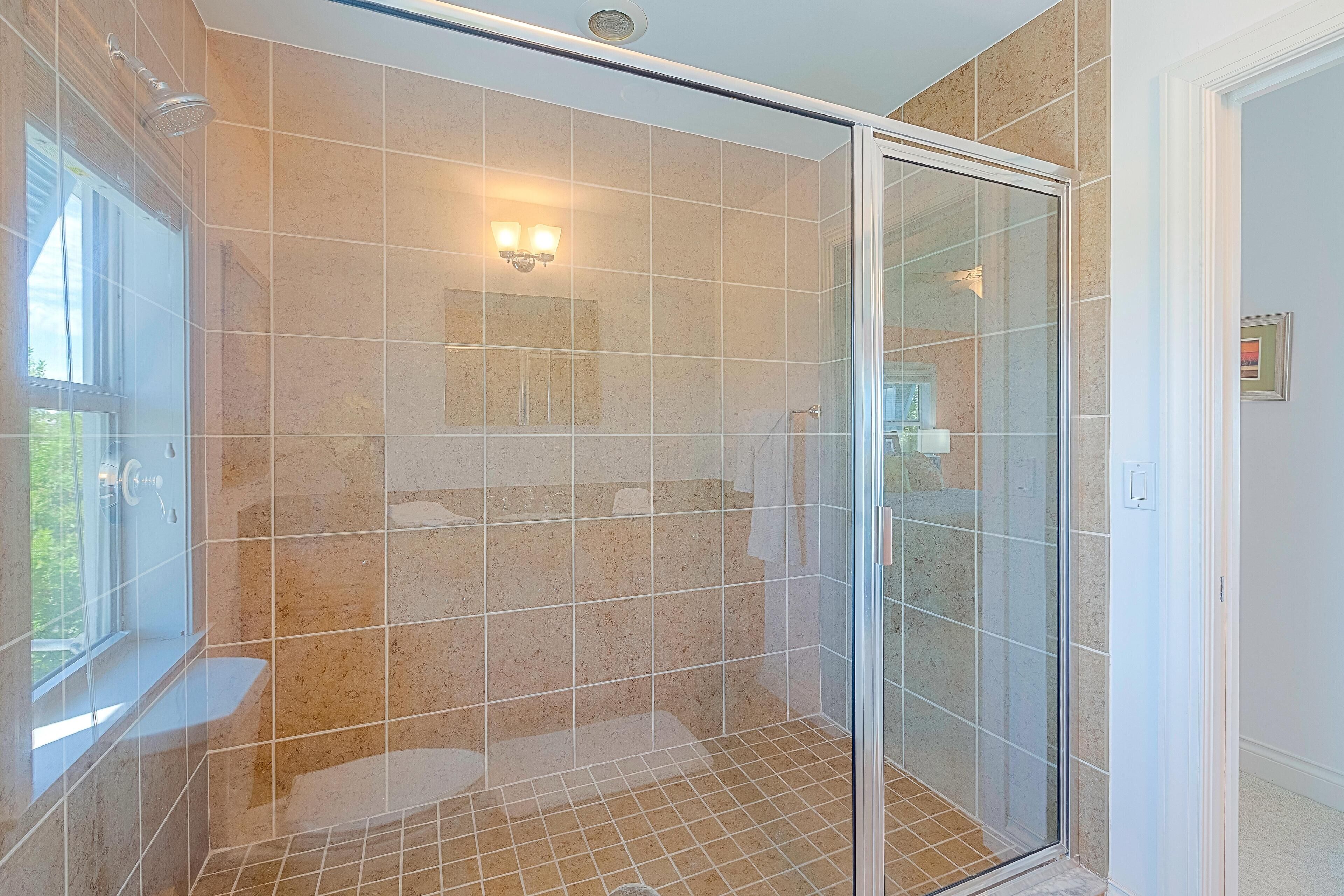 Un baño moderno con cabina de ducha de vidrio, baldosas color beige y un ventanal que proporciona luz natural.