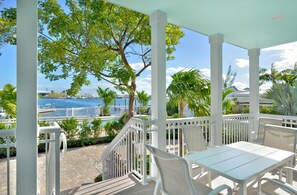 A covered outdoor seating area with white furniture, a view of the sea, and a white railing. - Bayview South 801 Eisenhower Dr. #6 (Key West)