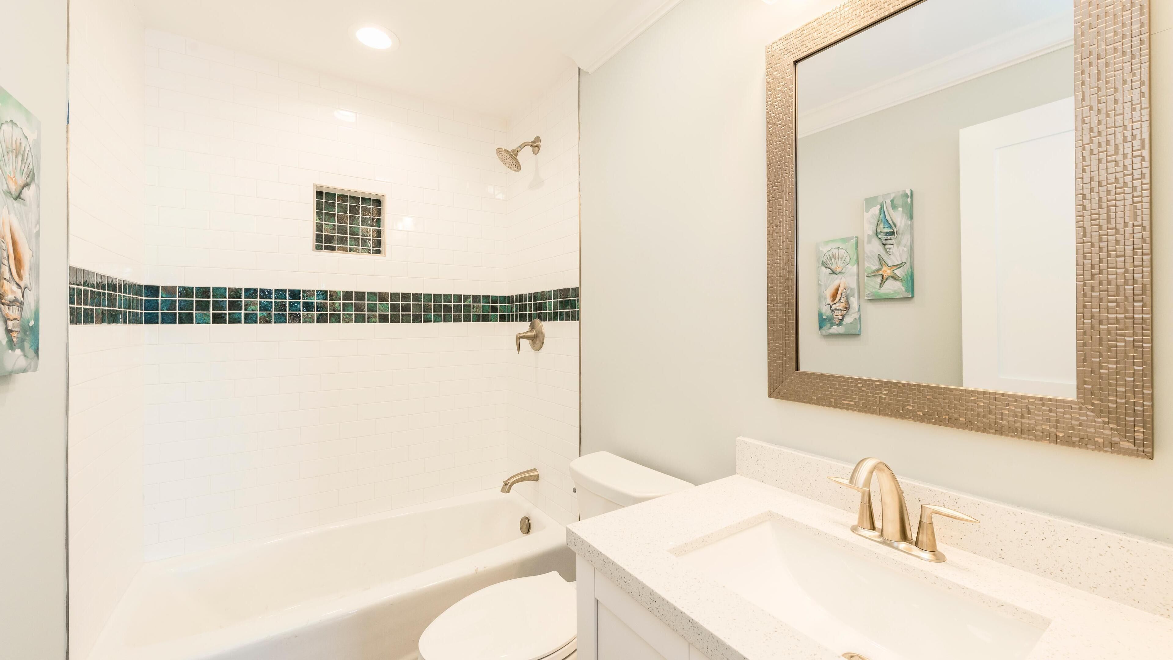 A bathroom with a bathtub, a sink with a gold faucet, and a mirror with a decorative frame.