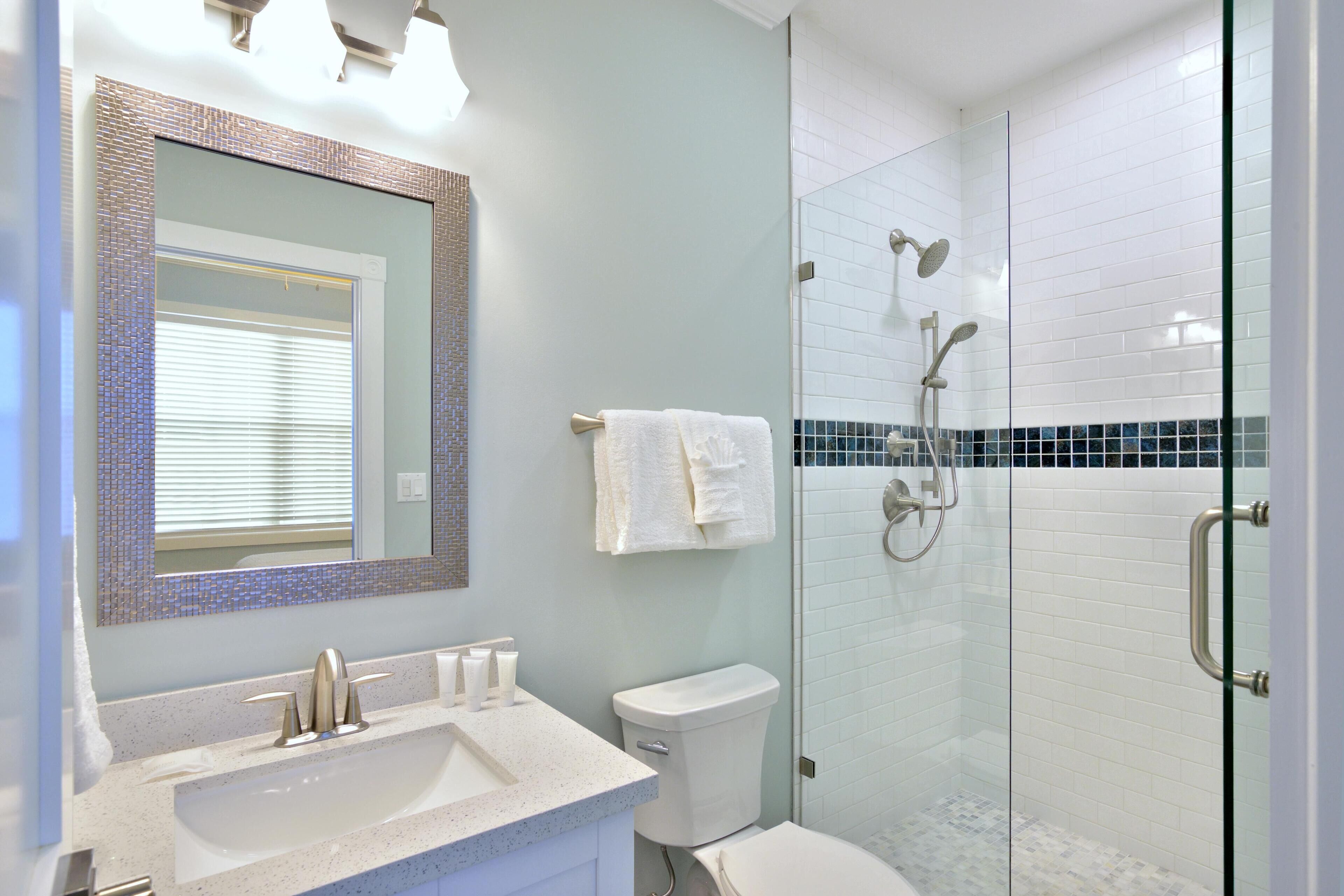 Une salle de bain avec une douche à parois de verre, un lavabo avec un miroir et des toilettes.