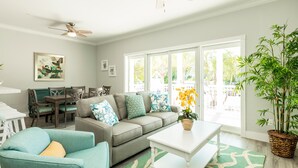 A spacious living room with a sectional sofa, a dining area with a table and chairs, and large windows offering a view of the outdoors. - Sunset North (Key West)