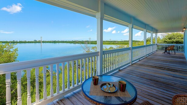 Une terrasse couverte avec vue sur un lac, une table ronde avec des chaises et une rambarde.