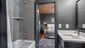 A modern bathroom with a bathtub, a shower, and a sink. There is a wooden floor and a bed visible through an open door. - Immaculate Meets Comfort! 3 BR Spacious Home! (Nashville)