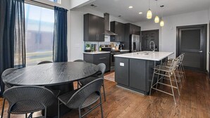 A modern kitchen with dark cabinetry, a central island, and a dining area with wicker chairs. - Immaculate Meets Comfort! 3 BR Spacious Home! (Nashville)
