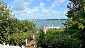 A dock leading to a body of water with a white picket fence and lush greenery. - Paris Mango (Key West)