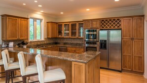 A modern kitchen with granite countertops, stainless steel appliances, wooden cabinets, and a bar area with stools. - Paris Mango (Key West)