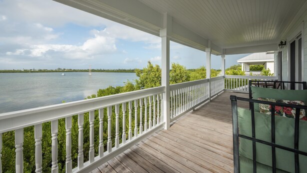 A covered wooden deck with white railings overlooking a body of water. - Paris Mango (Key West)