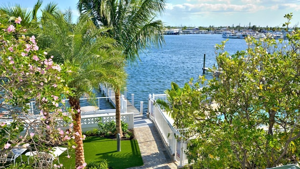 A waterfront property with a paved walkway leading to a dock, surrounded by lush greenery and palm trees. - Upper Sunset South (Key West)