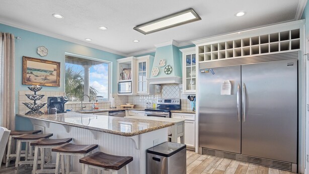 Una cocina con isla central, taburetes de bar, refrigerador de acero inoxidable y ventana con vistas.