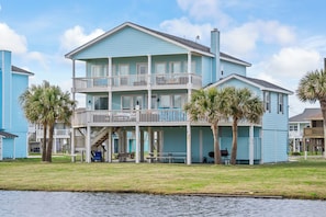 A two-story building with a balcony, palm trees, and a grassy area in front.