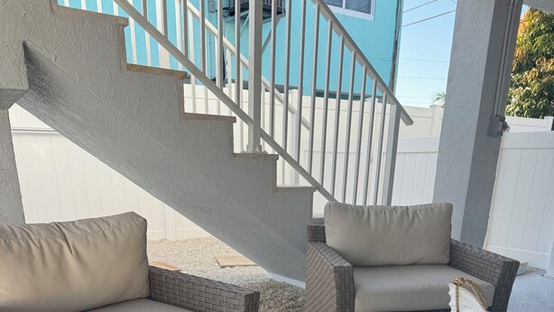 Un espace patio aménagé avec des meubles en osier, un tapis à rayures et un escalier.