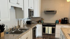 Une cuisine moderne avec des meubles blancs, un plan de travail en granit, des appareils électroménagers en acier inoxydable et un tapis à motifs.