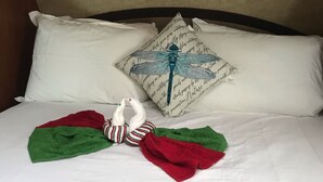Un lit bien fait, avec une couvre-lit à motifs, des oreillers et un coussin décoratif orné d’un motif de libellule.