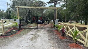Une entrée fermée par un portail en métal décoratif, entourée d’une clôture en bois et agrémentée de plantes.