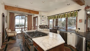 A spacious kitchen with a large island, built-in appliances, and large windows offering a view of the outdoors.