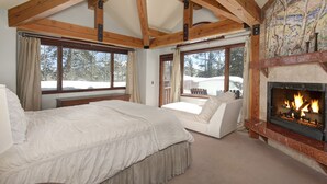 A bedroom with a large bed, a sofa, a fireplace, and windows with curtains.