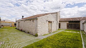 Un edificio de piedra con techo de tejas, patio cubierto de césped y un camino pavimentado.